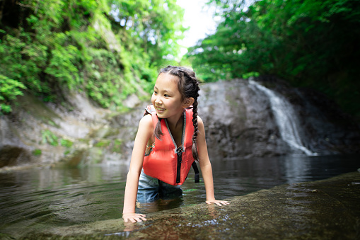 A girl wearing a life jacket and playing in the river