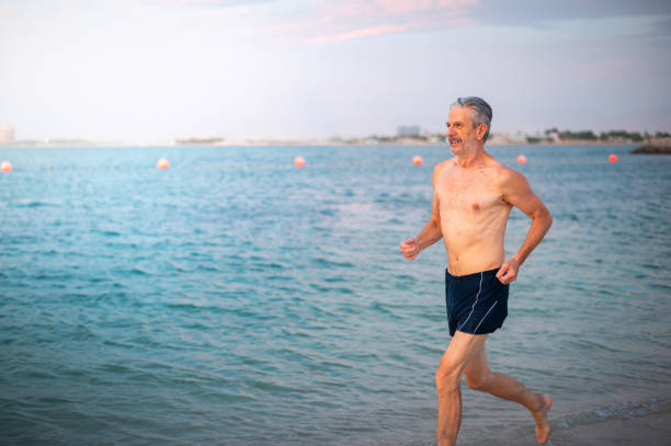 uomo anziano che corre in spiaggia per uno stile di vita attivo e sano e vacanze estive - men beach running shirtless foto e immagini stock