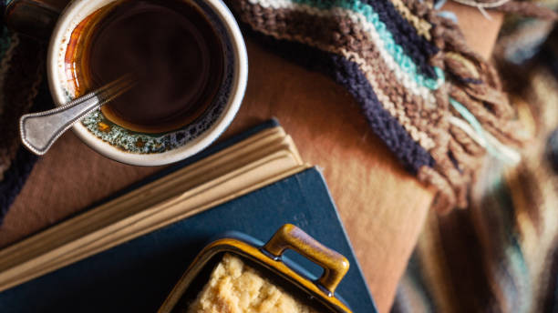Cosiness concept. Cup of coffee, plate with cake, book and warm scarf