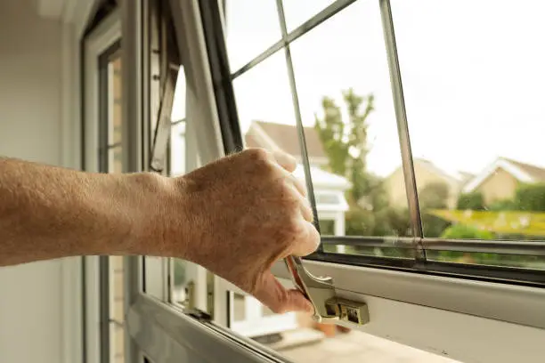 Photo of Homeowner seen about to lock a double glazed window seen on the ground level of a property.