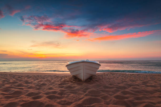 Tropical Seascape with a boat on sandy beach at cloudy sunrise or sunset