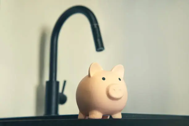 Photo of the rise in price of housing and communal services. Metal tap and piggy bank on sink. Water saving concept