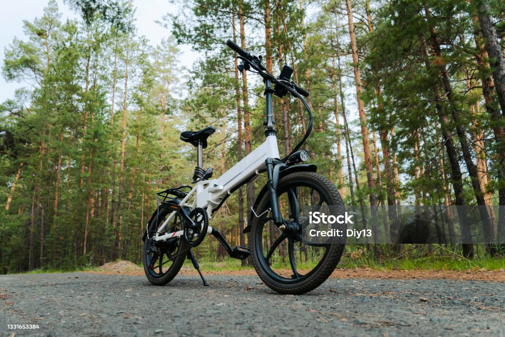 Eco friendly mode of transport. A bicycle with an electric motor. An electric bike of white color on the background of a green forest. Eco friendly mode of transport. bicycle with an electric motor. An electric bike of white color on the background of a green forest. Electric Bicycle Stock Photo