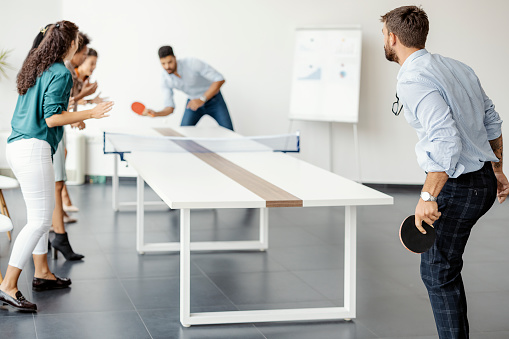 Young people playing table tennis in workplace, having fun. Concept of leisure activity, sport, friendship, team building, teamwork.