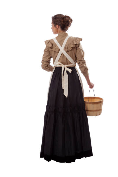 joven mujer de la pradera en delantal mirando hacia la izquierda y sosteniendo una canasta aislada sobre blanco - skirt brown fotografías e imágenes de stock