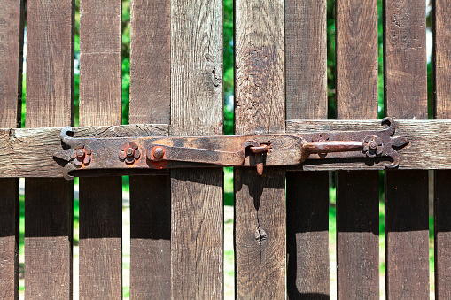 Espagnolette on a wooden gate . Old rusty lock of gate . Planks and rusty metal