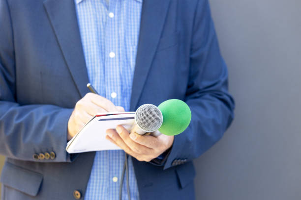 istock Journalist at media event or press conference, holding microphone, writing notes. Broadcast journalism concept. 1331663943