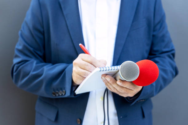 istock Journalist at news conference or media event, holding microphone, writing notes. Broadcast journalism concept. 1331666093
