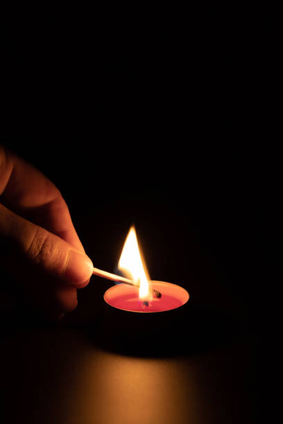 istock Lighting a red candle with a match in the dark. Memory concept. Black background, vertical orientation. 1331675439