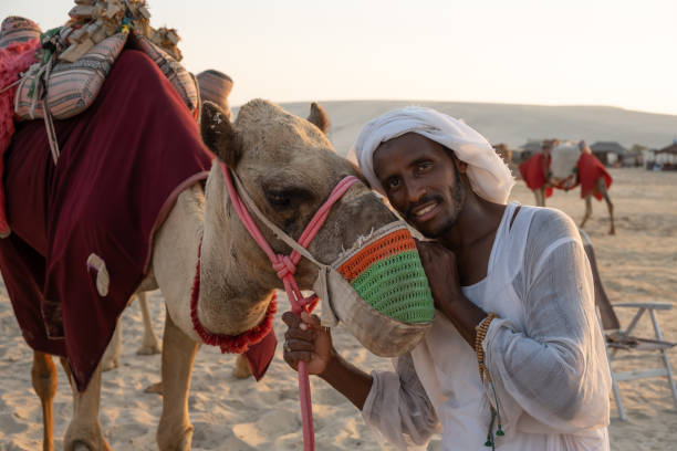 View of of a local man with his camel in Desert Safari Camel Ride camp, a landmark for desert activities, in Al Wakrah, Qatar. stock photo