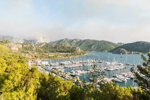 Marmaris, Mugla, Turkey - July 31, 2021. Orhaniye marina in Marmaris resort town of Turkey, with smoke from forest fires rising in the background