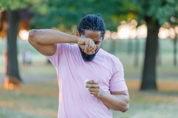 Allergic African Man is Rubbing his Eyes in the Park. An African-American Man with Sight or Allergy Problems is Rubbing his Eyes During the Walk in a City Park on Sunny Day. human eye scratching allergy rubbing stock pictures, royalty-free photos & images