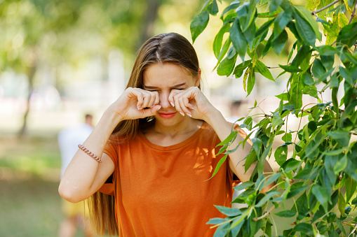 Young Woman with Eyes Problems is Feeling Displeased and Rubbing her Eyes During a Walk in City Park During a Summer Day.