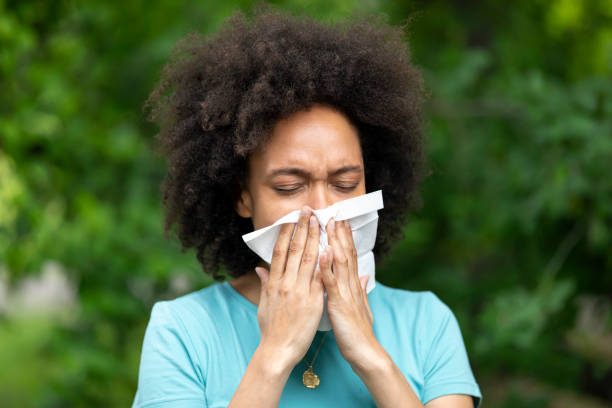 mujer joven africana con resfriado o gripe está sonando su nariz en el parque público. - sneezing tissue young adult cold fotografías e imágenes de stock