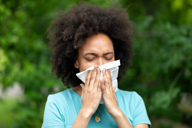 감기나 독감에 시달린 젊은 아프리카 여성이 공공 공원에서 코를 불고 있다. - sneezing tissue young adult cold 뉴스 사진 이미지