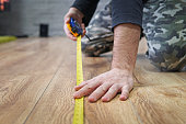 laying laminate flooring. Measurement of the area of the apartment. repair, building and home concept - close up of male hands measuring wood flooring