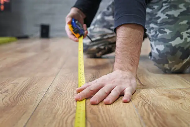 Photo of laying laminate flooring. Measurement of the area of the apartment. repair, building and home concept - close up of male hands measuring wood flooring