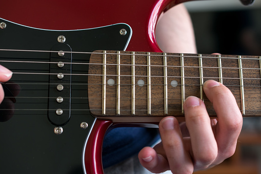 Close up view of a hand pressing the strings on an electric guitar, near the neck joint. Unrecognizable person playing the guitar, music concepts