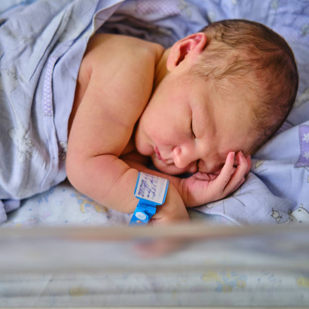 un neonato con un braccialetto dell'ospedale di maternità sul braccio sta dormendo in una culla. un neonato in un letto della clinica dietro un vetro trasparente - braccialetto di identificazione foto e immagini stock