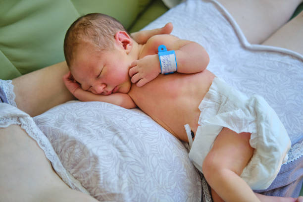 A mother is holding a newborn baby in her arms, with a maternity hospital bracelet on her arm. A newly born child in the clinic A mother is holding a newborn baby in her arms, with a maternity hospital bracelet on her arm. A newly born child in the clinic baby bracelet stock pictures, royalty-free photos & images