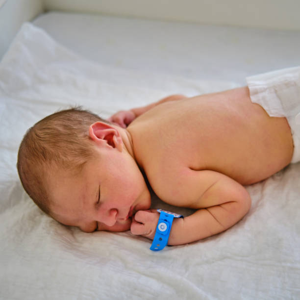 A newborn baby with a maternity hospital bracelet on his arm on a changing table A newborn baby with a maternity hospital bracelet on his arm on a changing table baby bracelet stock pictures, royalty-free photos & images