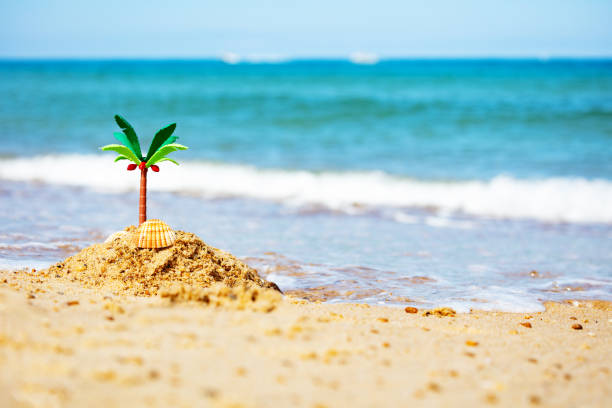 Miniature tiny toy sand island and palm tree close-up on the sea beach with waves passing