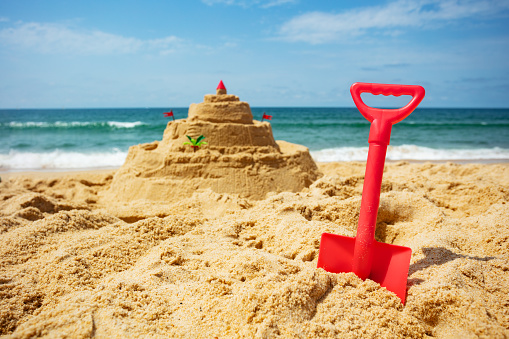 Toy scoop and sand castle on the beach with toys forms, many palm tree, sea on background