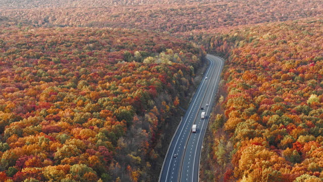 Highway in the mountains in the early morning, right after sunset, in the colorful fall season. Aerial drone video with the panning camera motion.