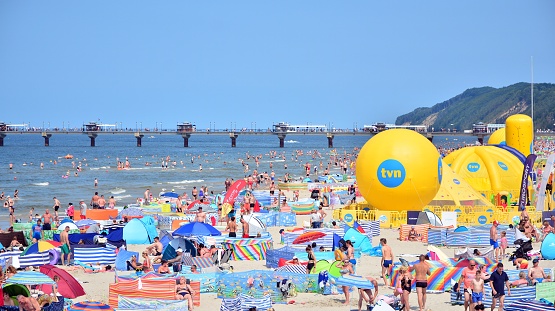 Miedzyzdroje, Poland. 22 July 2021. Tourists, sunbeds and windbreaks on summer hot day. Tourists on the beach on summer they sunbathe, rest and swim in the sea. The Miedzyzdroje pier in the background