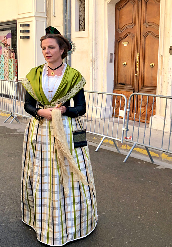 Vertical photo of a young woman from the city of Arles, standing in the street wearing traditional costume during May Day celebrations