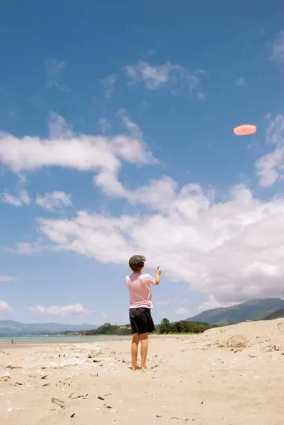 A young boy flies a stunt kite at the beach in summer.