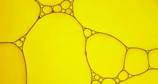 Abstract  of oil droplets patterns creating an art image with shadow effect caused by lighting and colour on golden-yellow coloured background.