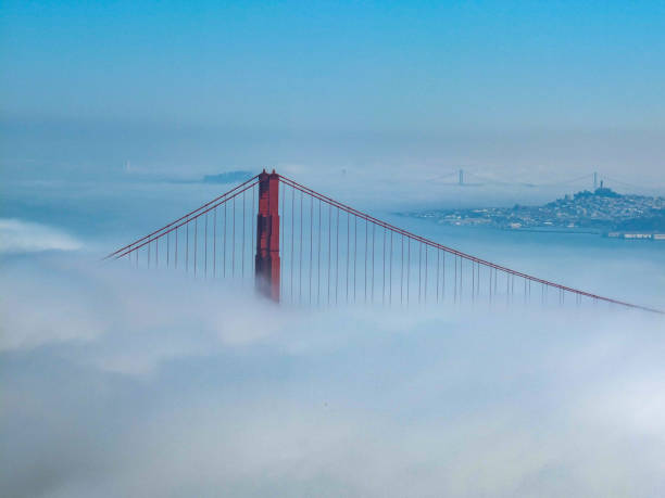 Golden Gate Bridge covered in fog with blue sky and Bay Bridge in the background