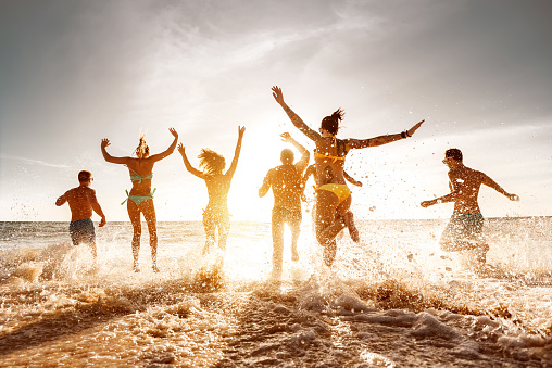 Big group of friends run and jump at sunset sea beach. Summertime holidays concept