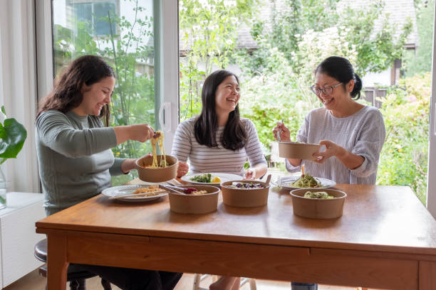 Eurasian Daughters and Chinese Mother Eating Vegan Takeout Meal Together stock photo