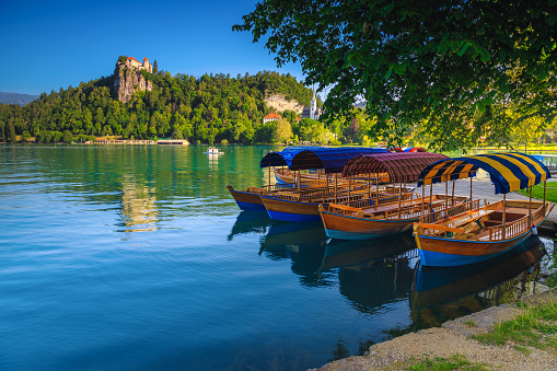 Traditional touristic wooden Pletna boat moored on the waterfront. Pletna rowing boats on the alpine Bled lake and medieval fortress on the cliffs in background, Slovenia, Europe