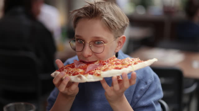 Little boy eating delicious Italian pizza at a restaurant.