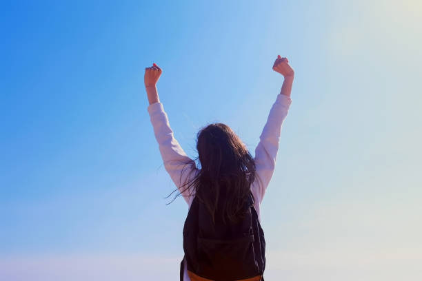 istock Girl winner in victory pose with raising hands on sky background back view. 1331743420
