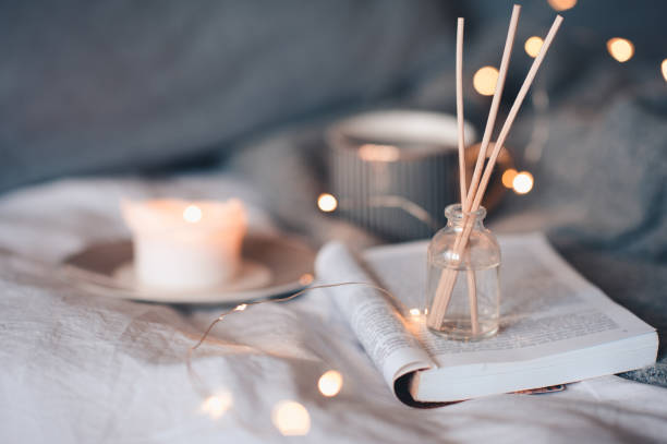 Liquid home perfume with candle in bed Bottle with liquid home fragrance and wooden bamboo sticks, scentes burn candle and cup of black tea over glow lights at background close up. Winter holiday season. Cozy romantic home atmosphere. home diffuser stock pictures, royalty-free photos & images