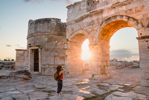 Photographer tourist girl is taking photos of the Frontinus Gate in ancient ruins in Hierapolis , Pamukkale