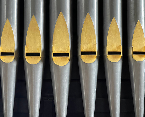 Row or rank of polished Organ Pipes from a pipe organ, a musical instrument producing sound by driving pressurized air through the individually pitched pipes.  Each set or rank of pipes has a common timbre and volume enabling a variety of sounds to be selected from a keyboard