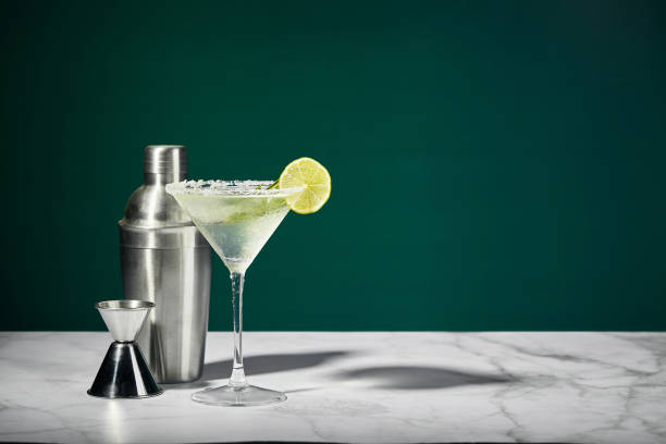 Martini cocktail with ice and slice of lime and shaker on a marble table. An alcoholic cocktail or non-alcoholic mocktail. Martini cocktail with ice and slice of lime, and shaker on a marble table. An alcoholic cocktail or non-alcoholic mocktail martini stock pictures, royalty-free photos & images