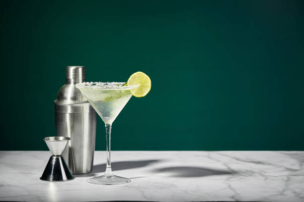 coquetel martini com gelo e fatia de limão e shaker em uma mesa de mármore. um coquetel alcoólico ou um mocktail não alcoólico. - copo de martini - fotografias e filmes do acervo