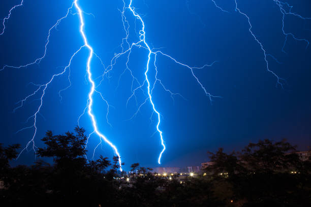 scariche di fulmini durante un grande temporale in una città con frange forestali - lightning foto e immagini stock