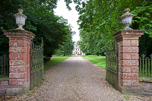 Buckshaw House entrance gates and driveway, Holwell, Dorset, England, UK. Distinctive grand country mansion architecture and mellow stone combine to create a property of style and outstanding beauty constructed at the end of an imposing tree-lined drive in the rolling Dorset countryside