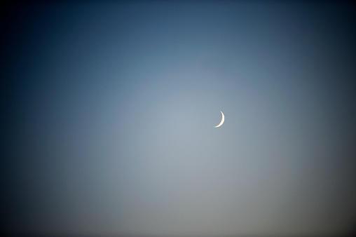New Moon appears as a sliver of silver in the twilight sky where details of the moon's craters can still be seen on its periphery on July 10th 2021 at sunset