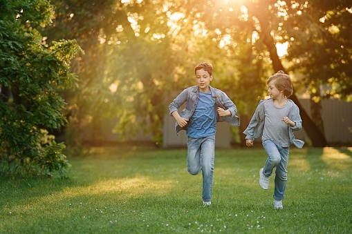 Two boys running and racing each other outdoors in park. Siblings connection