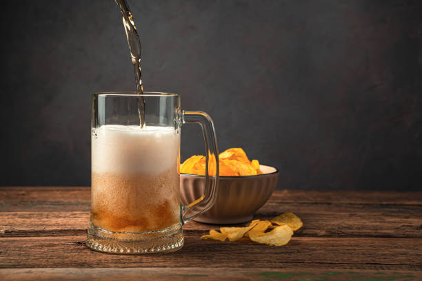 pouring beer into a beer glass on the background of potato chips - action alcohol alcoholism bar imagens e fotografias de stock