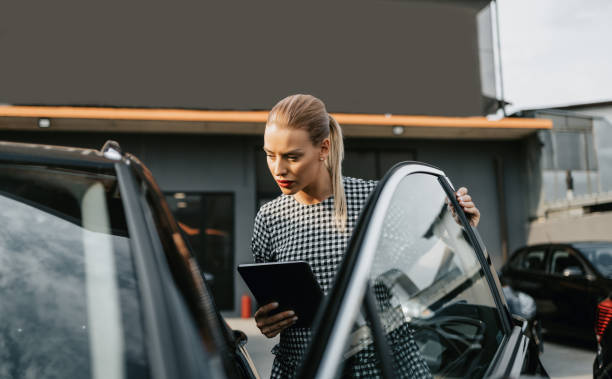 Female used car dealer checking vehicle before customer Beautiful young woman working as used car seller. She is using digital tablet and checking car condition before customer or buyer. Used vehicle dealership. showroom photos stock pictures, royalty-free photos & images