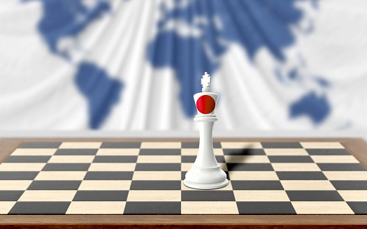 Japanese chess king covered with country flag is on a wooden chess board on table against world map background. Easy to crop for all your social media and design need with copy space.